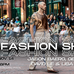 A photograph of an Indigenous man walking down a pedestrian street-turned-runway lined with onlookers. He wears long white tassel earrings, a bronze metallic leather vest, beige and blue pants, and brown loafers.