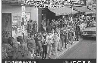 Black and white photo of people standing in a line on the sidewalk in front of stores.