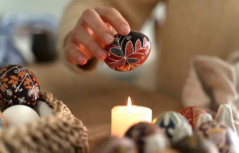 Female hand holding a pysanka egg above the candle