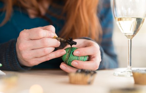 Woman writing pysanka egg on the tabletop next to the wine glass