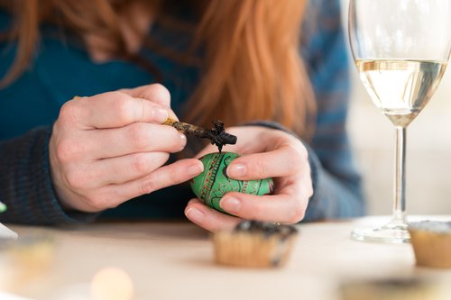 Woman writing pysanka egg on the tabletop next to the wine glass