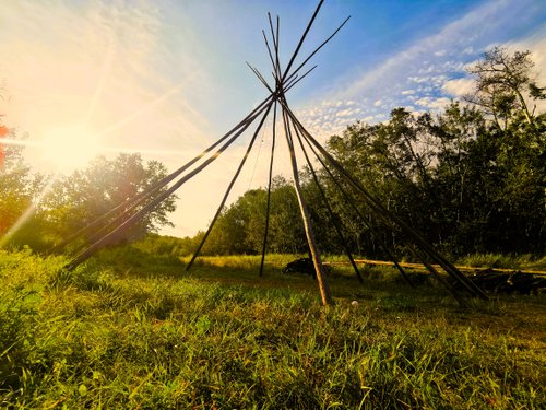Tipi poles with no canvas in a setting surrounded by trees